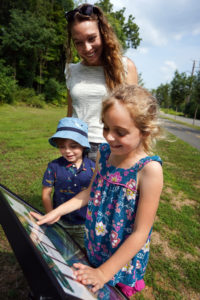 Walking along the Rappahannock Heritage Trail, Stephanie Gardner and her kids, Piper and Pierce, read ‘Alex’s Day on the Rappahannock,’ written and illustrated by students in UMW’s College of Education, as part of Fredericksburg Parks, Recreation and Events department’s new StoryWalk(R) project. Photo by Suzanne Carr Rossi.