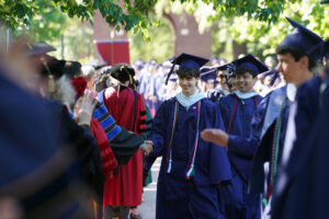 Graduates walk through campus on their way to Ball Circle for this year’s commencement ceremony, including Martina Nicholson who’s wearing the “feet” of the school’s Sammy D. Eagle mascot. Photo by Suzanne Carr Rossi.