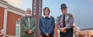 A student, professor and Chief of Police stand in front on one of the University's blue light phones.