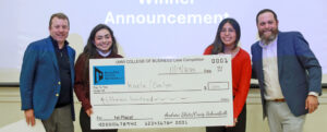 Two students and two adults pose holding a $1,500 check for winning the fall 2025 College of Business Case Competition.