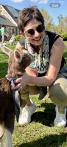 Woman wearing sunglasses poses with baby goat.