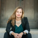 photo of woman sitting on steps in green blazer who is Associate Professor of Religious Studies Jennifer Barry