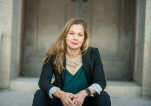 photo of woman sitting on steps in green blazer who is Associate Professor of Religious Studies Jennifer Barry
