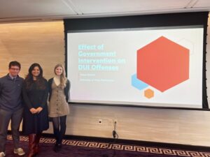 A photo of three people standing next to a presentation on a screen. Photo includes Josiah Schlechty, Tressa Ballard and Dr. Dhar at the conference in front of Tressa's presentation.