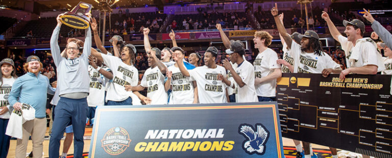Photo of UMW players and coach on the court holding the trophy from winning the national championship game