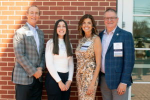 Photo of four adults posing in front of a red brick wall