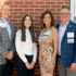 Photo of four adults posing in front of a red brick wall