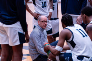 Photo of Coach Kahn kneeling with players in a huddle on the court