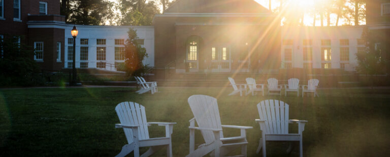 The sun comes up on campus showing Adirondack chairs clustered together in a grassy area