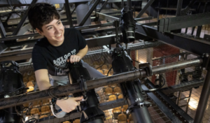 A student sets up lighting in the rafters of the theatre