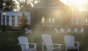 The sun comes up on campus showing Adirondack chairs clustered together in a grassy area