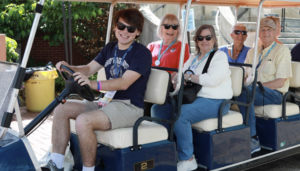 A student and several alumni in a golf cart on campus