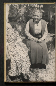 Grayscale photographic print of Gertrude Stein (right) sitting in a garden next to Alice B. Toklas (left)