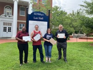 Four people stand with laptops in front of Lee Hall on UMW campus