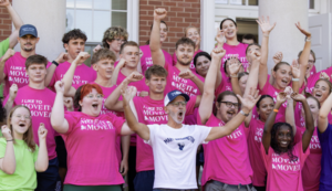 large group of students in mostly pink t-shirts on the steps of a campus building