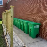 a line of green composting bins lined up outside a brick building on campus at UMW