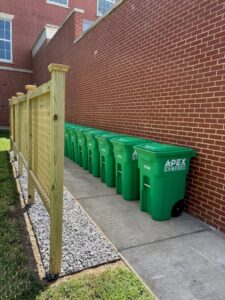 a line of green composting bins lined up outside a brick building on campus at UMW