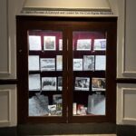 Display of memorabilia on glass shelf inside a display case with red velvet backing