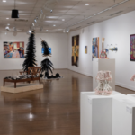 a gallery at the University of Mary Washington with displays of artwork and sculpture, including two arching trees and a chaise chair