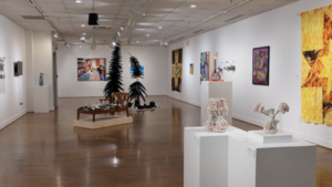 a gallery at the University of Mary Washington with displays of artwork and sculpture, including two arching trees and a chaise chair