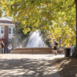 student walk outdoors in front of a fountain and brick building on the campus of the University of Mary Washington