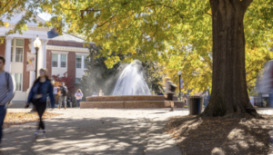 student walk outdoors in front of a fountain and brick building on the campus of the University of Mary Washington