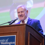 man with jacket and tie speaks into a microphone behind a podium