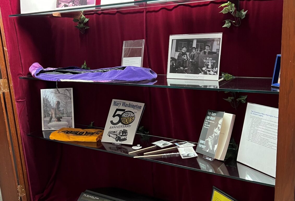 Display of memorabilia (like letters, photos, and books) on glass shelves inside a case with red velvet backing