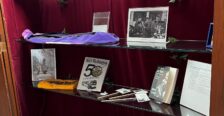 Display of memorabilia (like letters, photos, and books) on glass shelves inside a case with red velvet backing