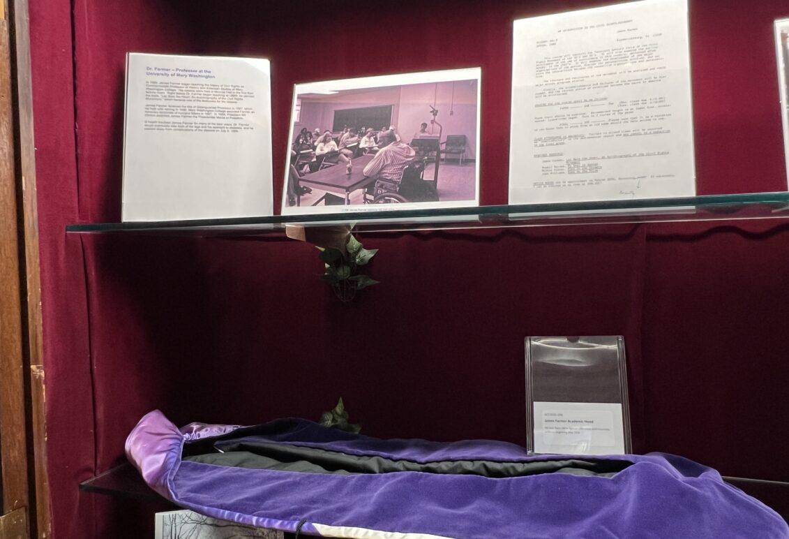 Display of memorabilia, like letters and photos, on glass shelf inside a case with red velvet backing