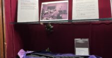 Display of memorabilia, like letters and photos, on glass shelf inside a case with red velvet backing