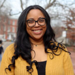 Woman with dark hair and yellow sweater stands outdoors