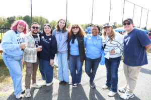 men and women stand arm in arm at the homecoming tailgate event