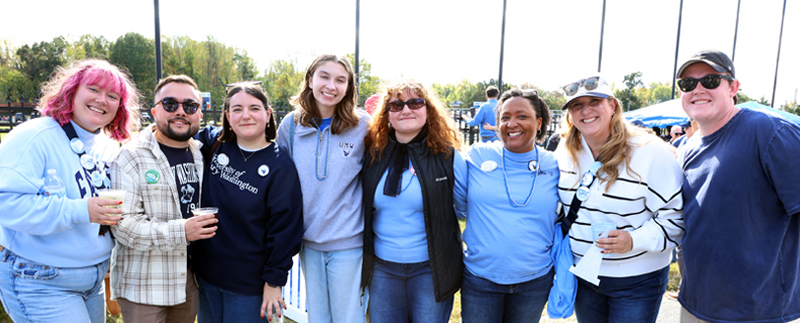 men and women stand arm in arm at the homecoming tailgate event